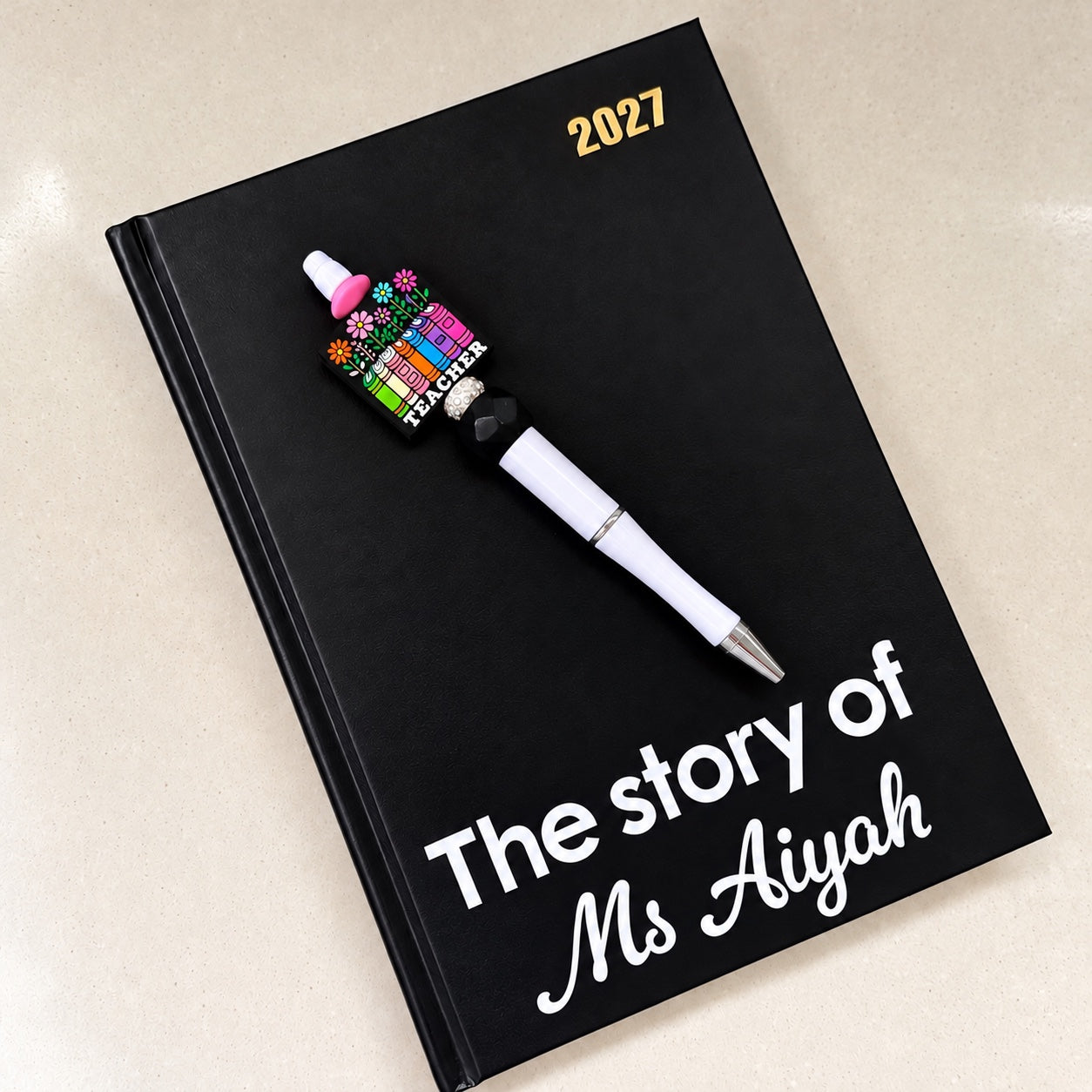 Personalised black 2027 teacher diary with colourful teacher-themed pen and custom name